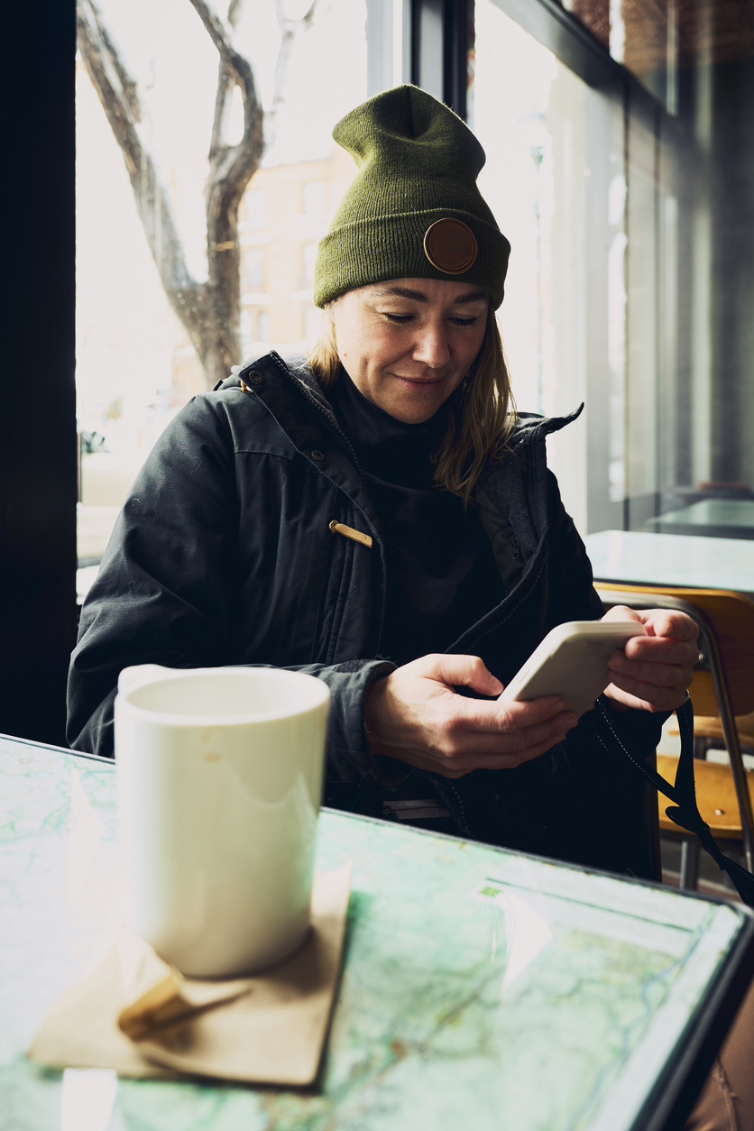 A woman sits at a cafe and is using her phone to view a website. She is smiling, signaling a good experience.